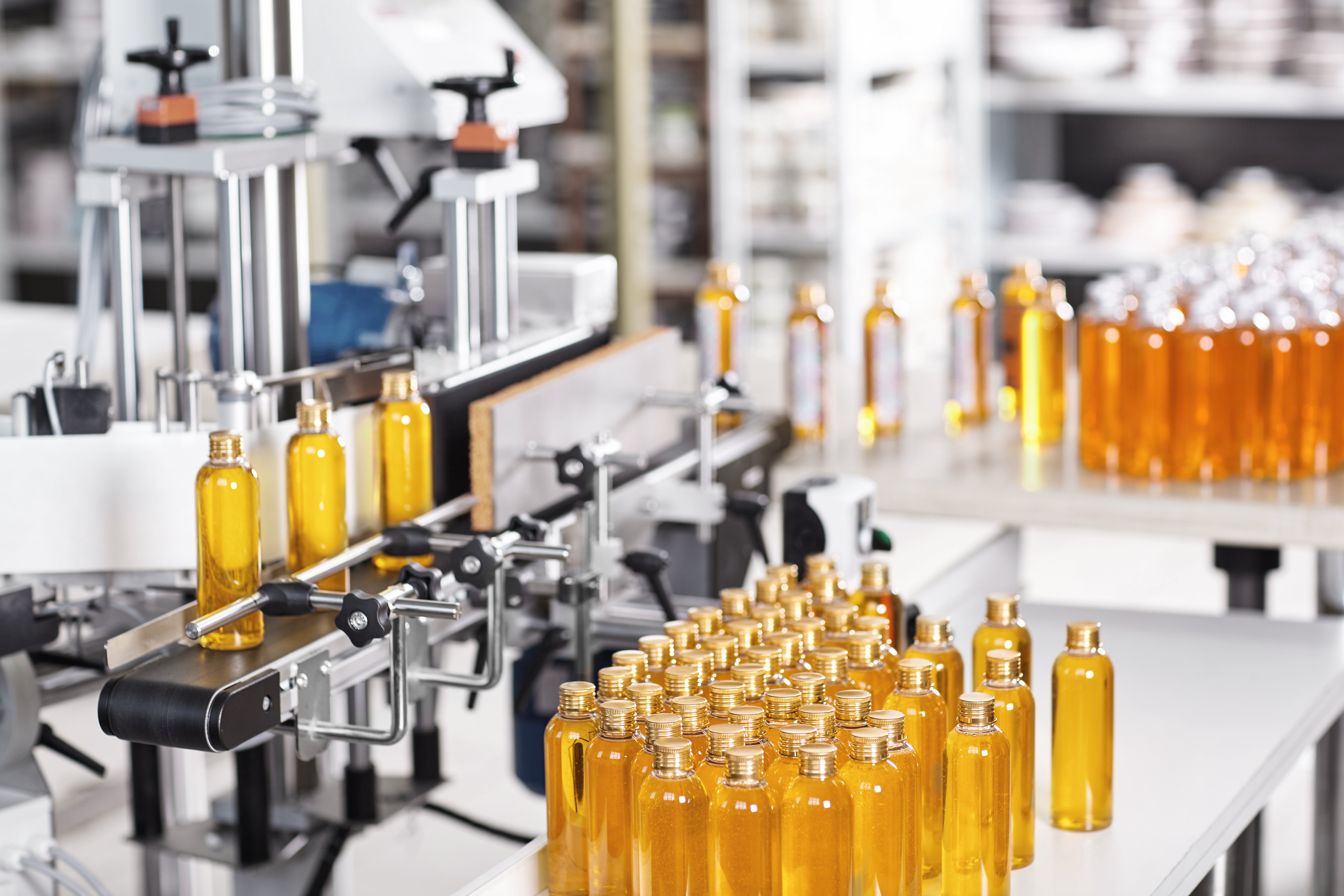 Bottles filled with yellow thick substance standing on desk and conveyor line.